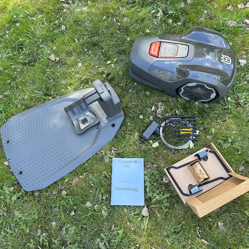 Husqvarna Automower Aspire R4 och alla tillbehör som följer med liggandes på en gräsmatta